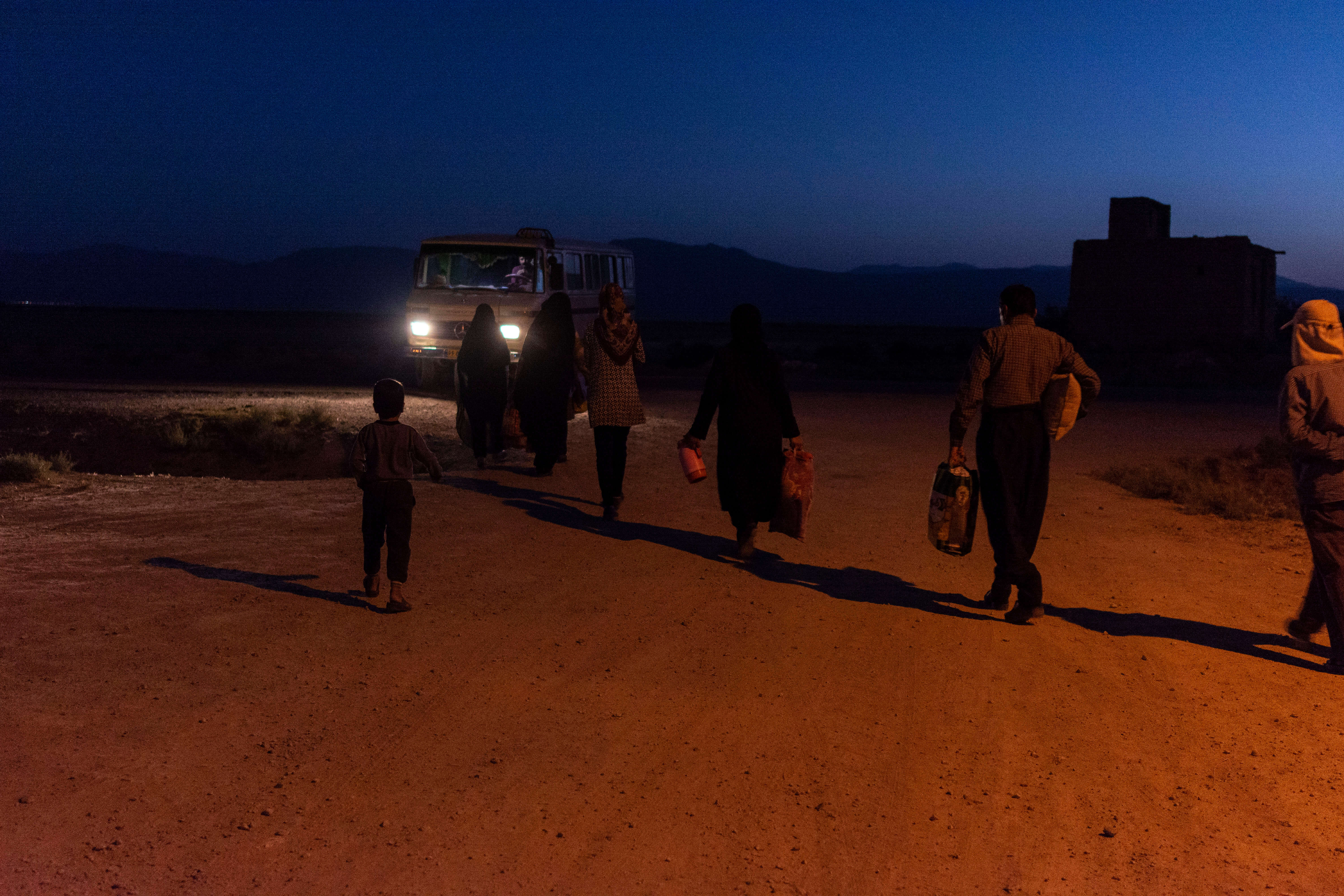Workers and their children are getting on the minibus to work in tomato farms of Arsenjan at five in the morning.Farmers of Korbal and Kharameh who have lost their farmland go to Arsenjan to harvest tomatoes in the summer and autumn. They wake up five in the morning. The distance from the farm to home of most of workers is more than 50 km. her daily wages are 60,000 tomans (equals to 4.5 US dollars) a day, for twelve hours of hard work. Nosrat village, Kharameh, Fars, Iran, August, 2018.